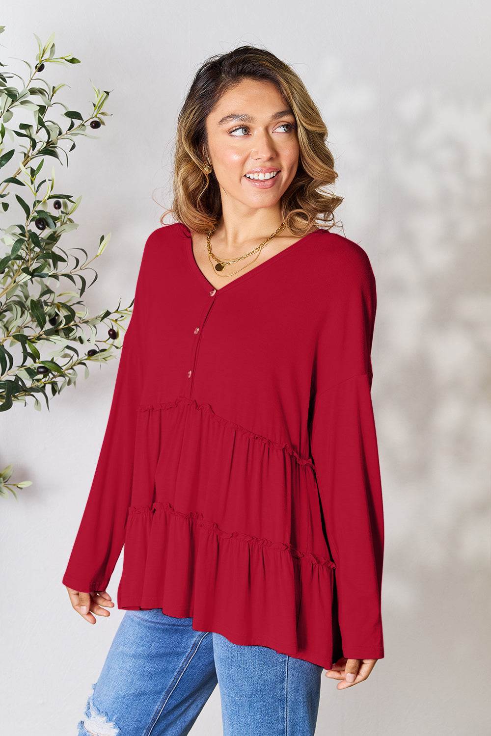 Woman wearing a red half button long sleeve ruffle hem blouse with blue jeans.