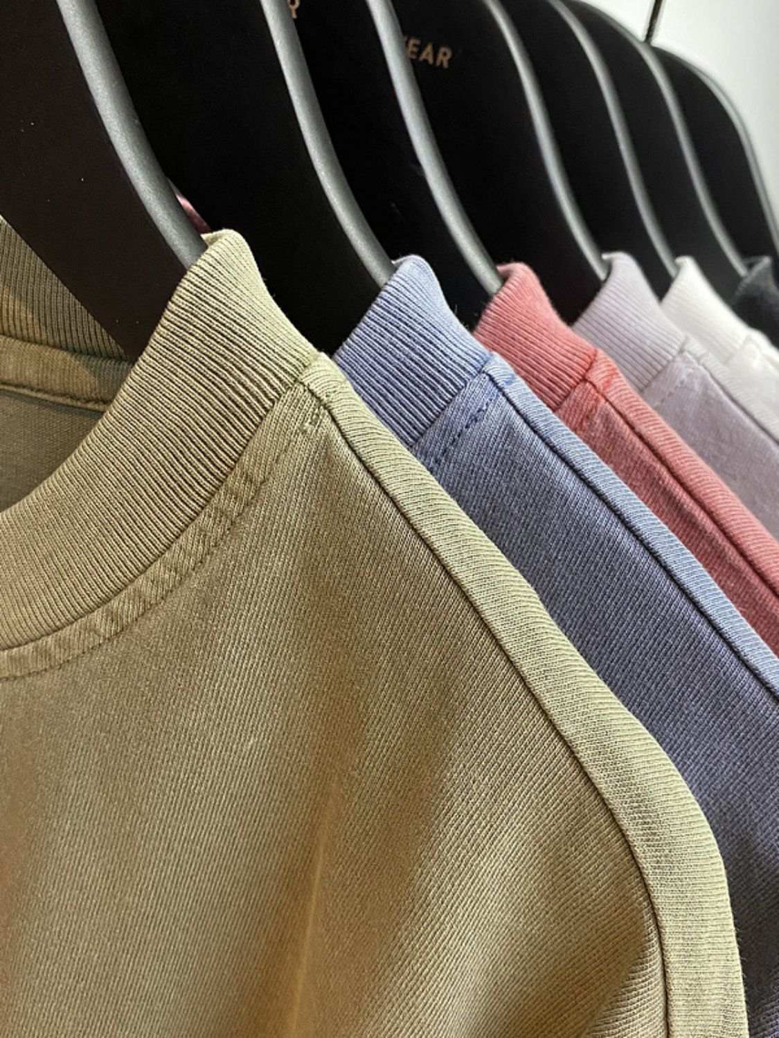 Men's round neck t-shirts in various colors hanging on black hangers.
