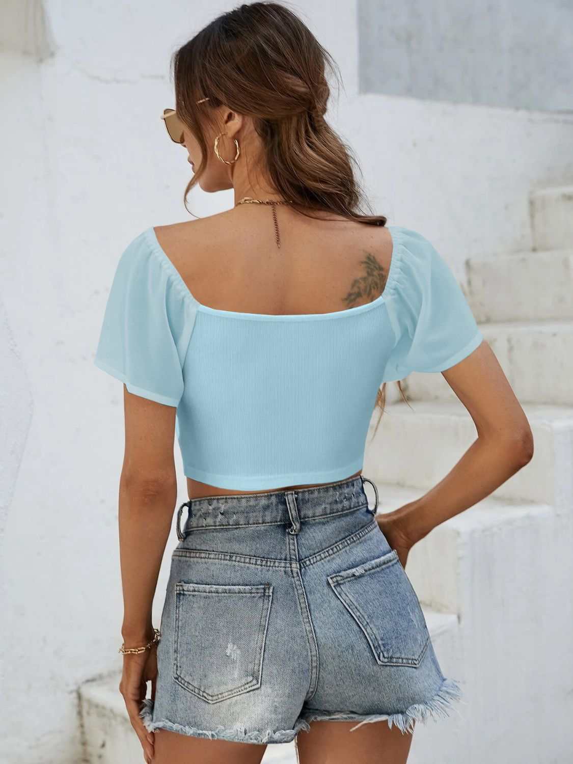 Woman wearing blue drawstring short sleeve crop top with denim shorts.