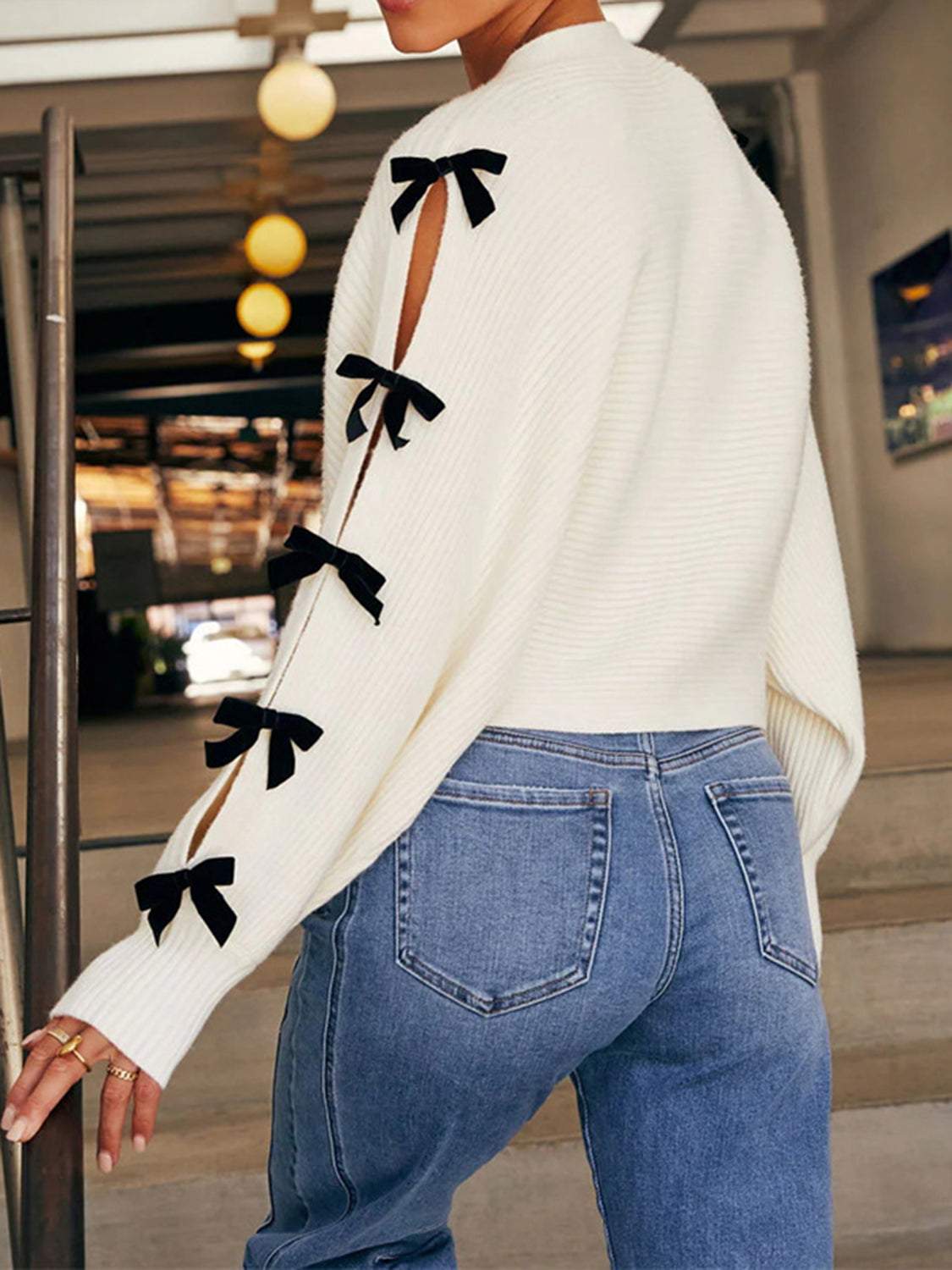 White V-neck cardigan with cutout sleeves, black bow details, and buttoned closure.