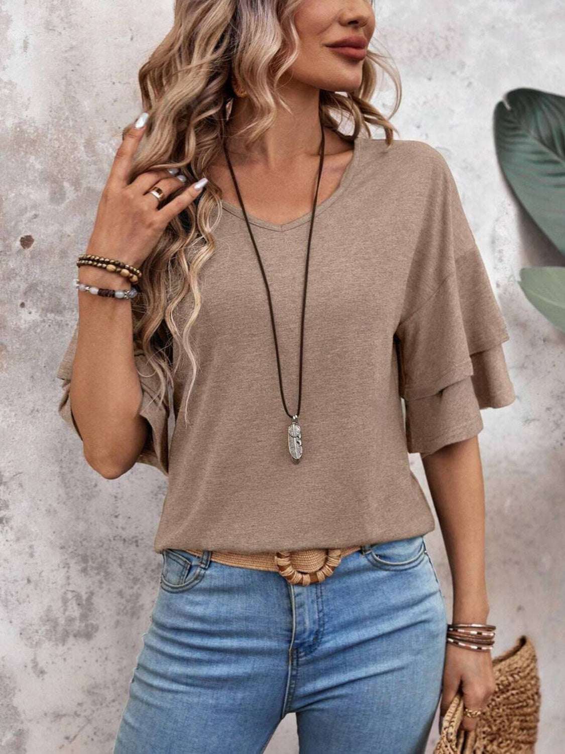 Woman wearing a V-neck half sleeve blouse with light wash jeans, accessorized with layered necklaces and bracelets.