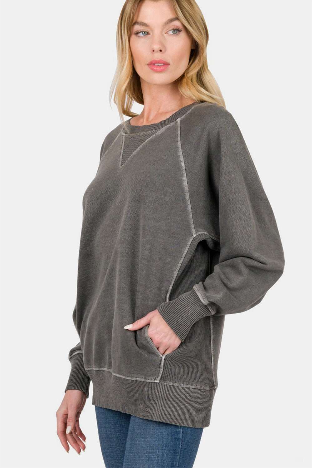 Woman wearing a charcoal gray Zenana round neck long sleeve sweatshirt with ribbed cuffs and hem.