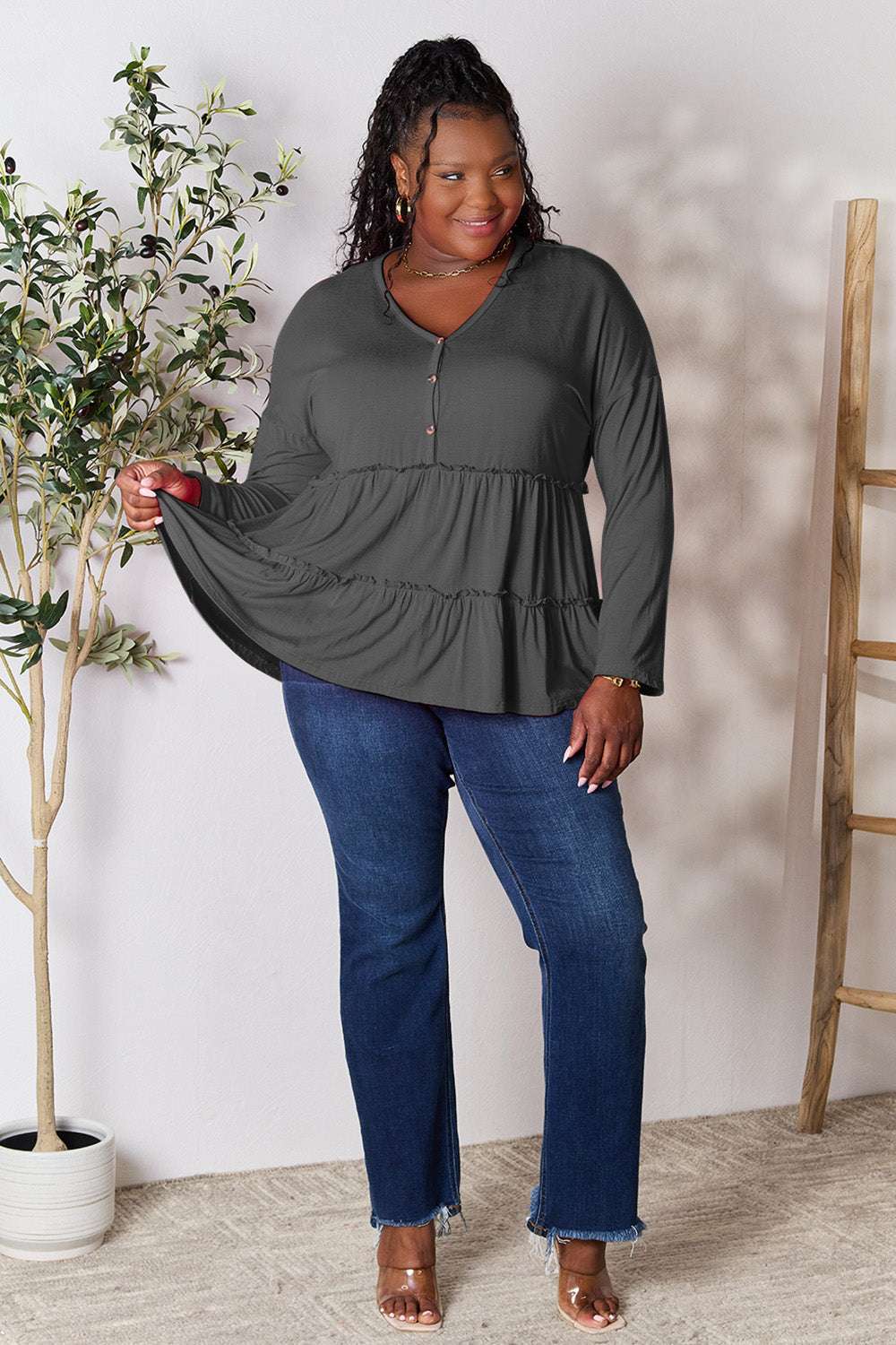 Black long sleeve blouse with ruffle hem and half button front, worn by a smiling model, paired with jeans.