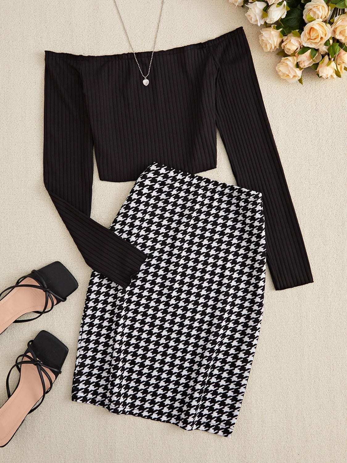 Off-shoulder long sleeve black ribbed top paired with black and white houndstooth skirt set displayed flat with black strappy heels and floral decor