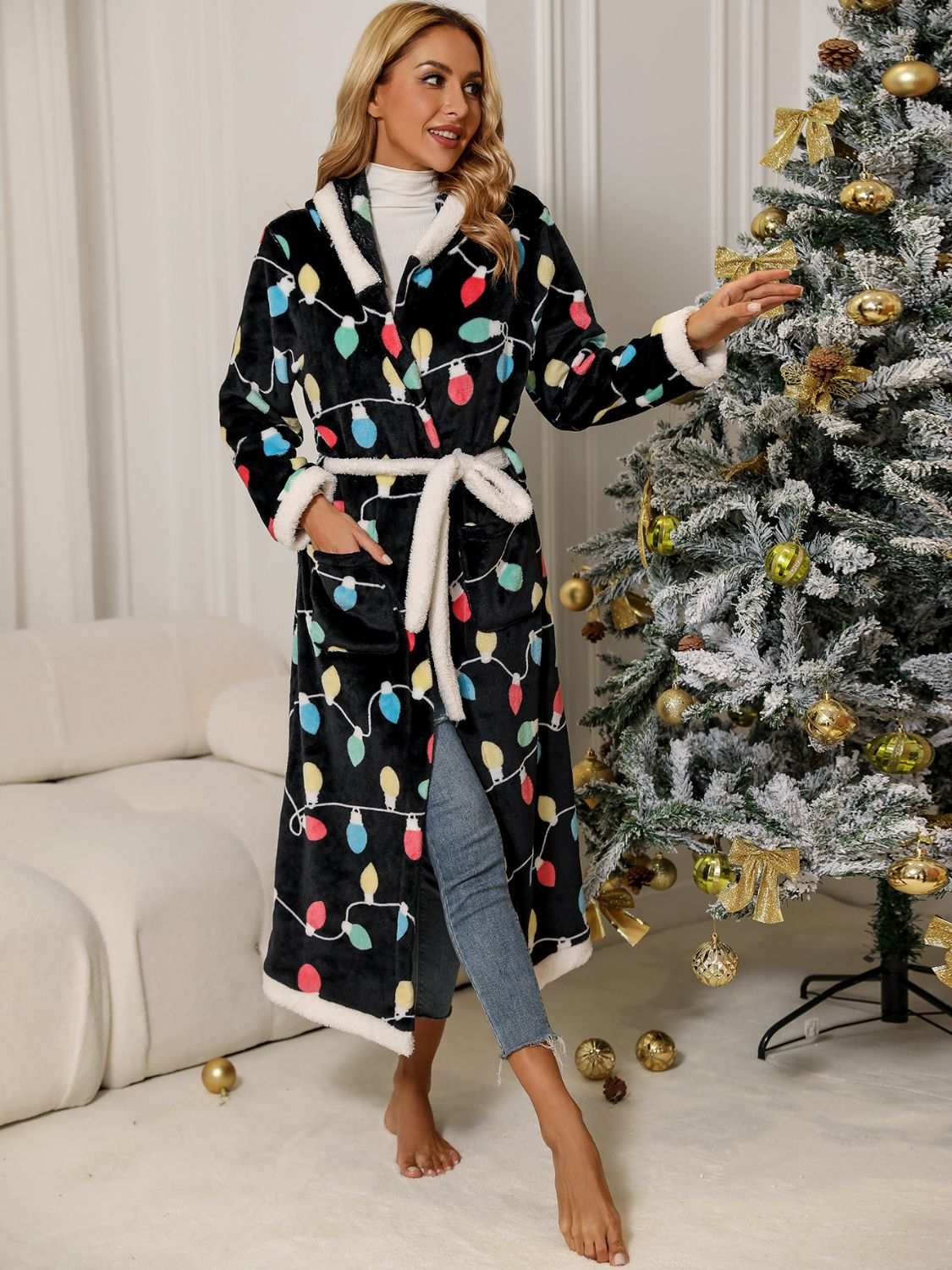 Woman wearing a tie waist hooded robe with colorful design, standing by a decorated Christmas tree.