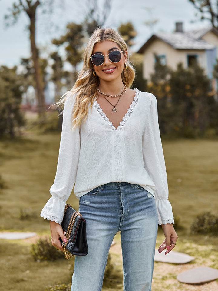 Woman wearing white V-neck flounce sleeve blouse with lace detail and blue jeans outdoors
