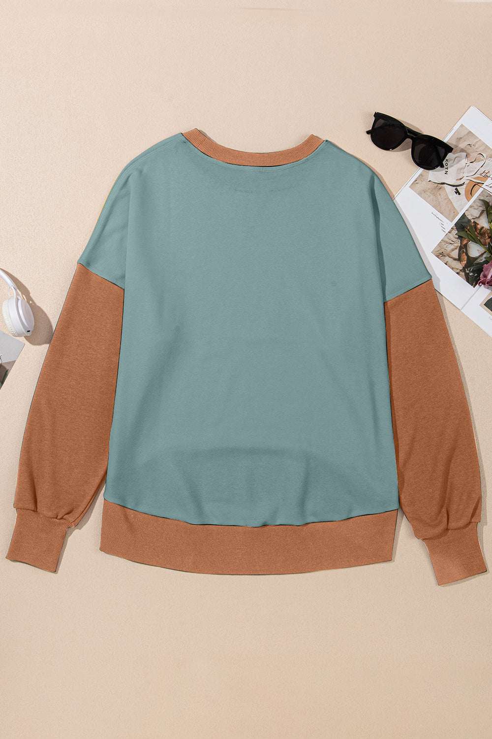 Contrast round neck long sleeve sweatshirt with teal body and brown sleeves on a beige background.