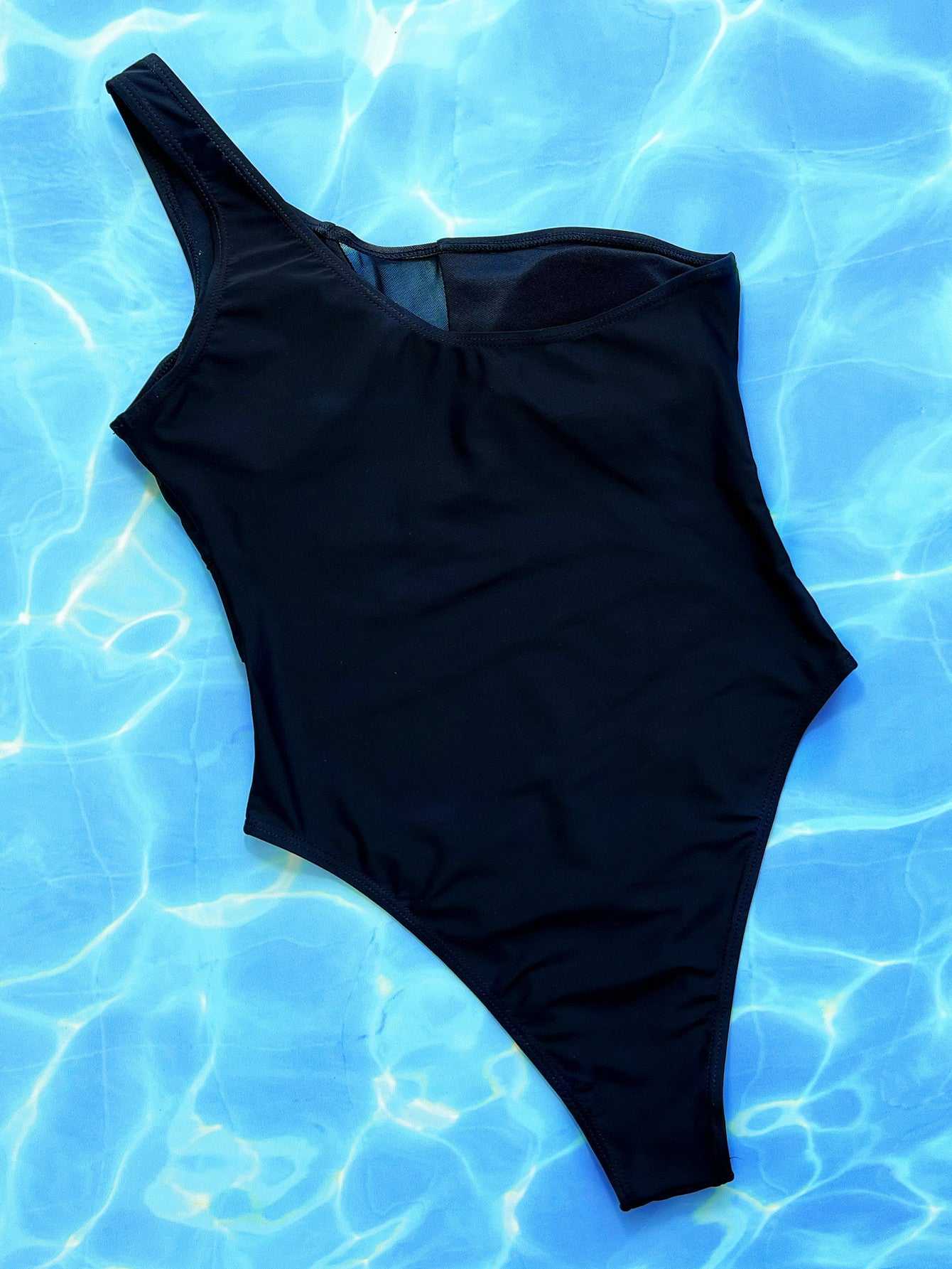 One-shoulder sleeveless black one-piece swimsuit on a blue water background.