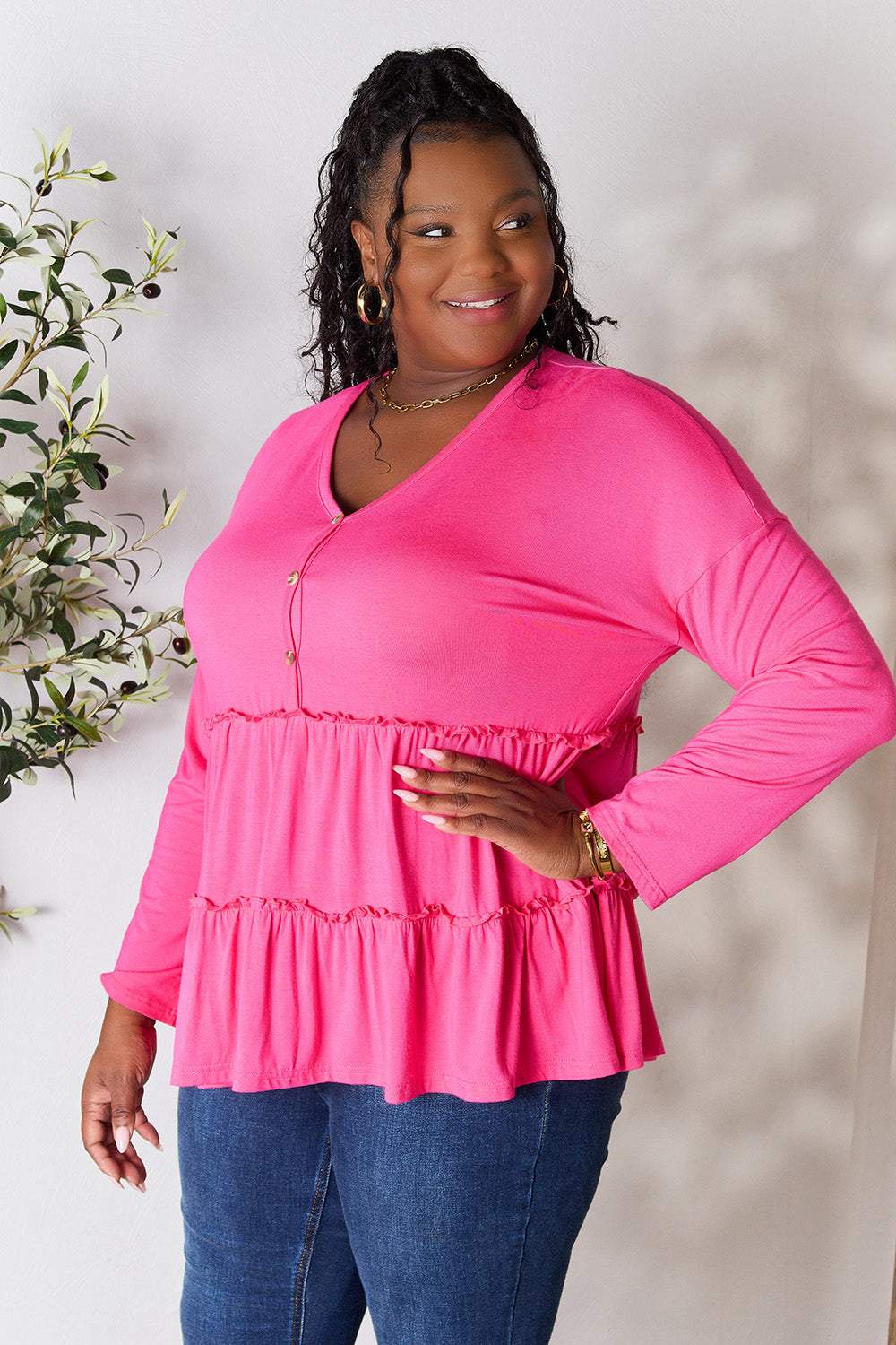 Curve model wearing a pink half button long sleeve ruffle hem blouse.