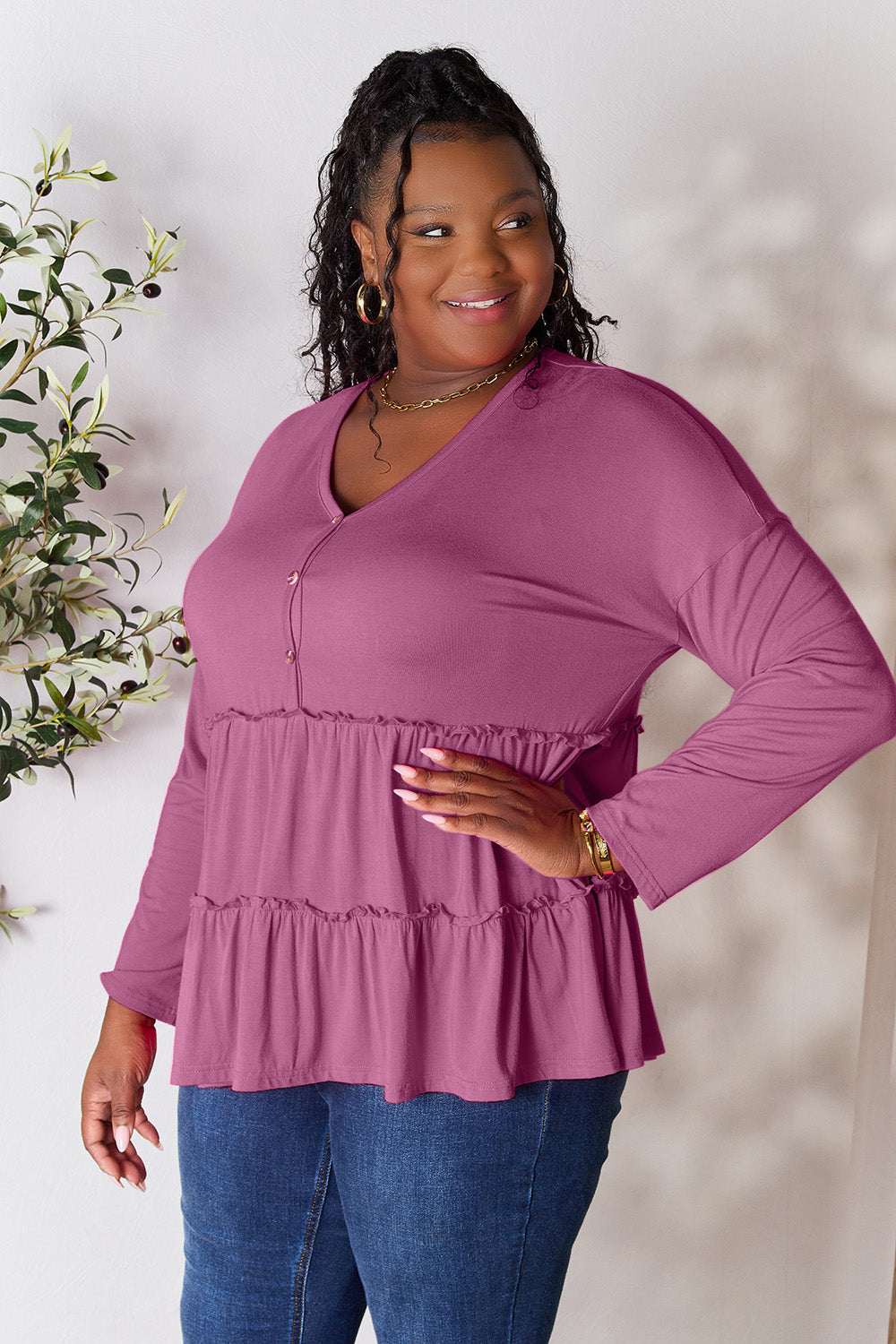 Curve model wearing a mauve half-button long sleeve blouse with ruffle hem.