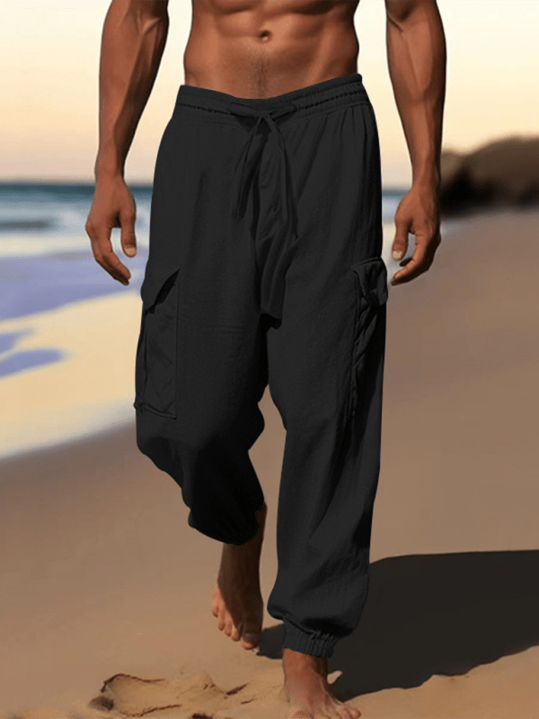 Casual cuffed multi-pocket drawstring trousers, solid black, 100% cotton, beach setting.