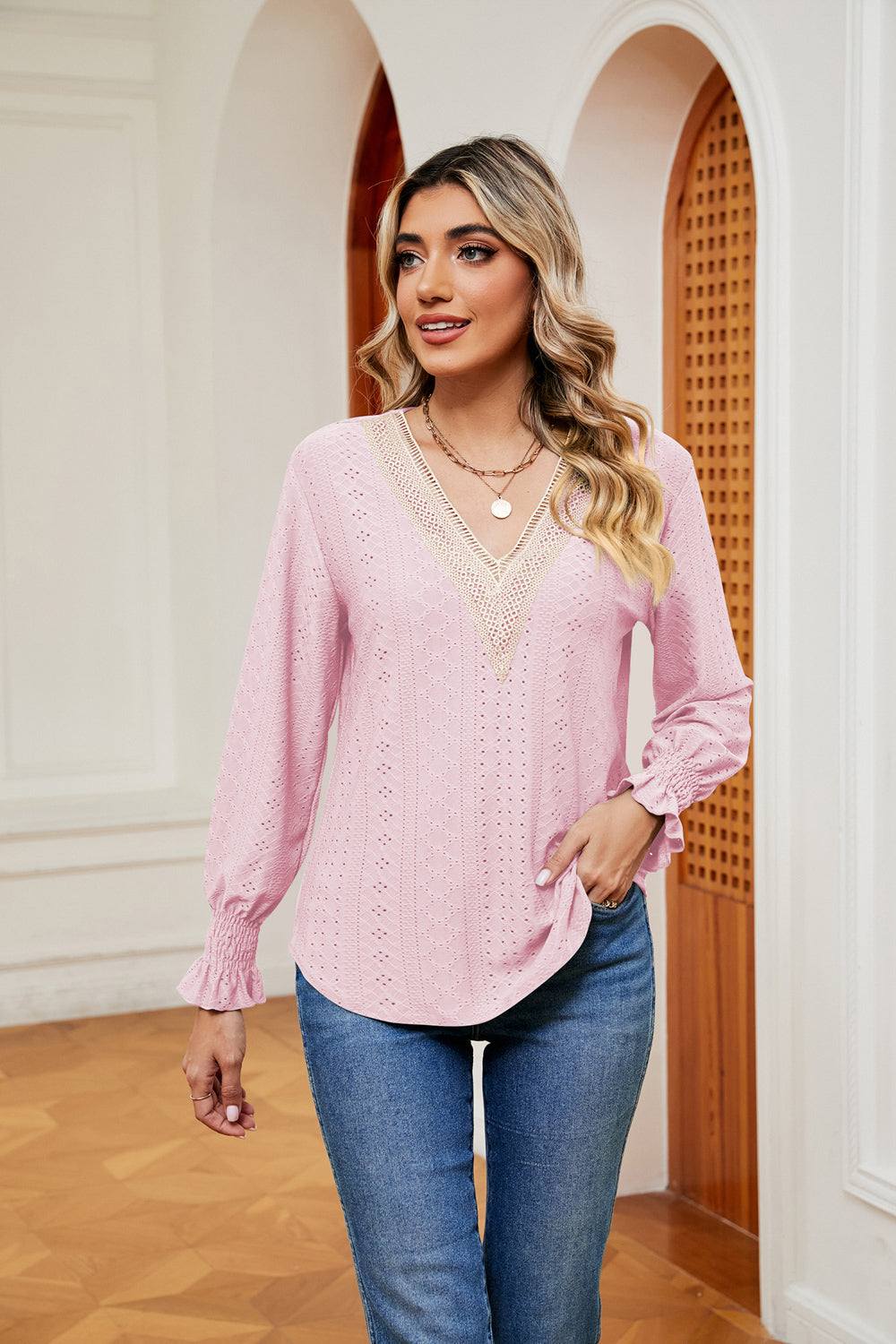 Woman wearing light pink contrast flounce sleeve blouse with V-neck and lace detailing paired with blue jeans indoors