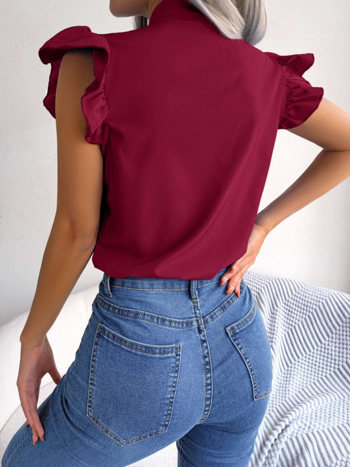 Woman wearing a red tie neck cap sleeve blouse with jeans.