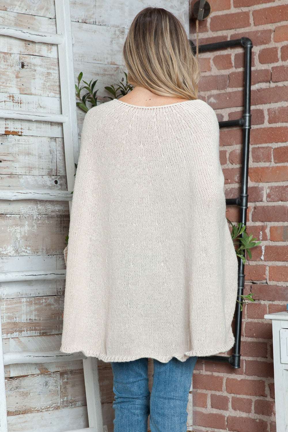Round neck batwing sleeve sweater in cream, slightly stretchy polyester, worn by a woman standing against a rustic backdrop.