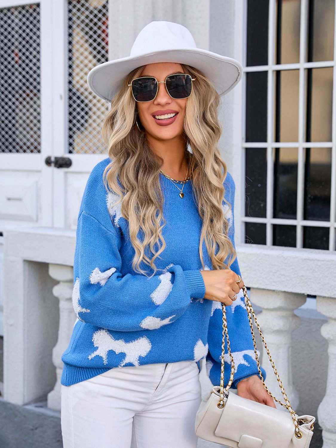 Blue angel wings sweater with bow design, round neck, and dropped shoulders, styled with white pants and a hat.