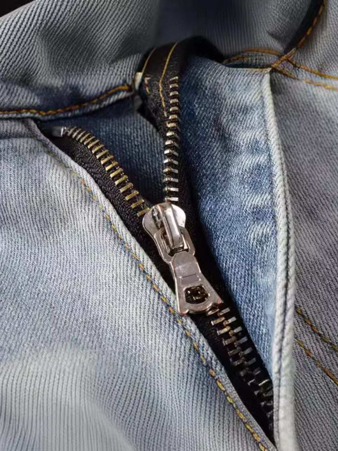 Close-up of zipper detail on men's distressed jeans with pockets.