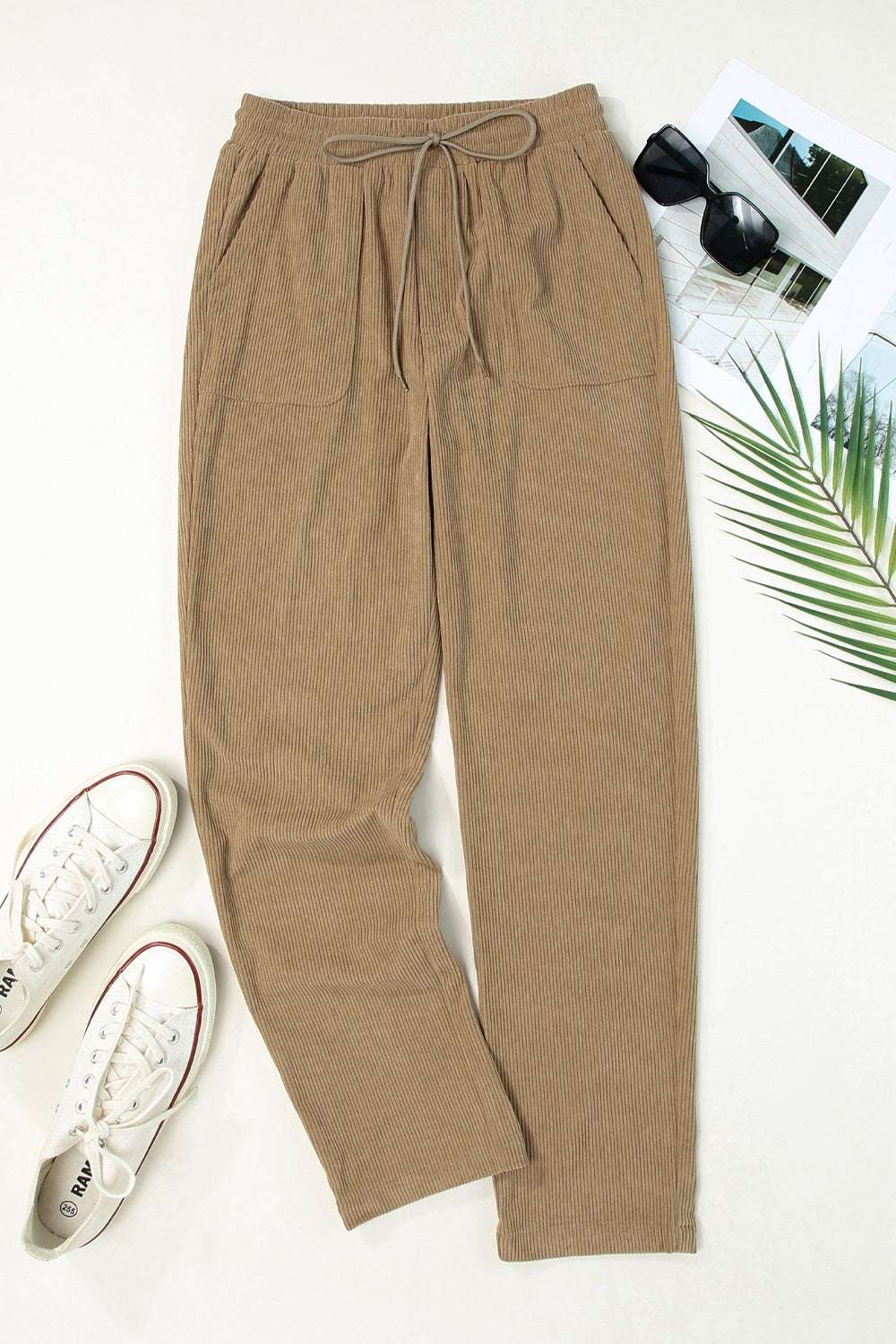 Drawstring straight pants with pockets made of 100% polyester, shown in a flat lay with casual sneakers and sunglasses.