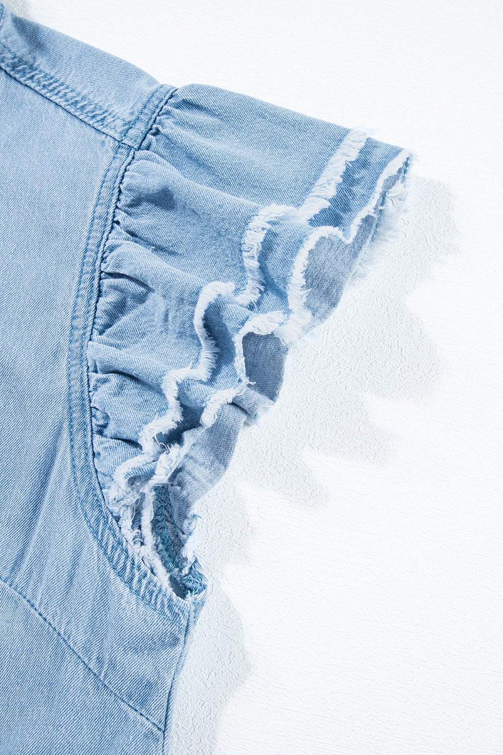 Ruffled sleeve detail of button down raw hem denim shirt.