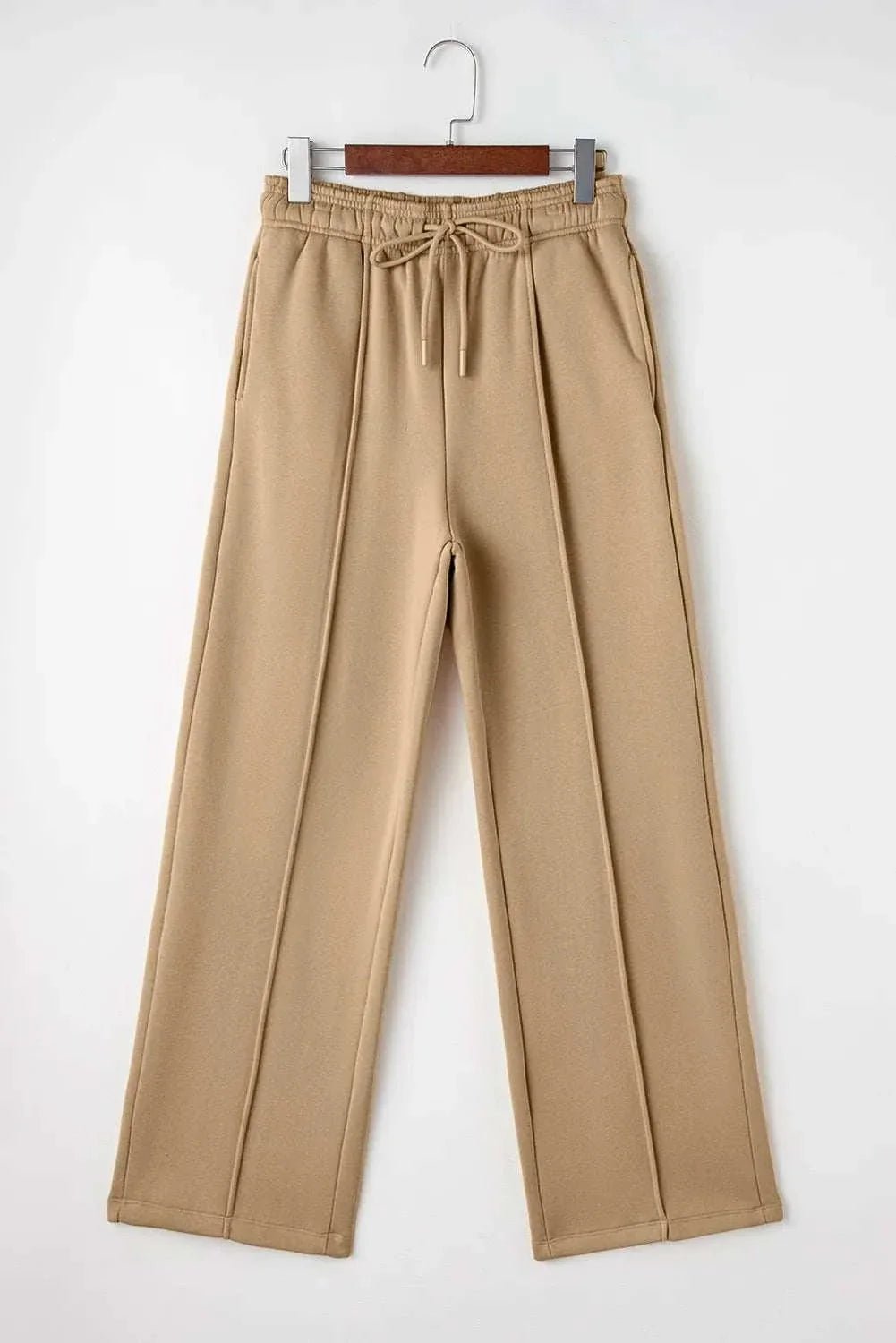 Drawstring wide leg pants with pockets in beige fabric hanging on a wooden hanger.