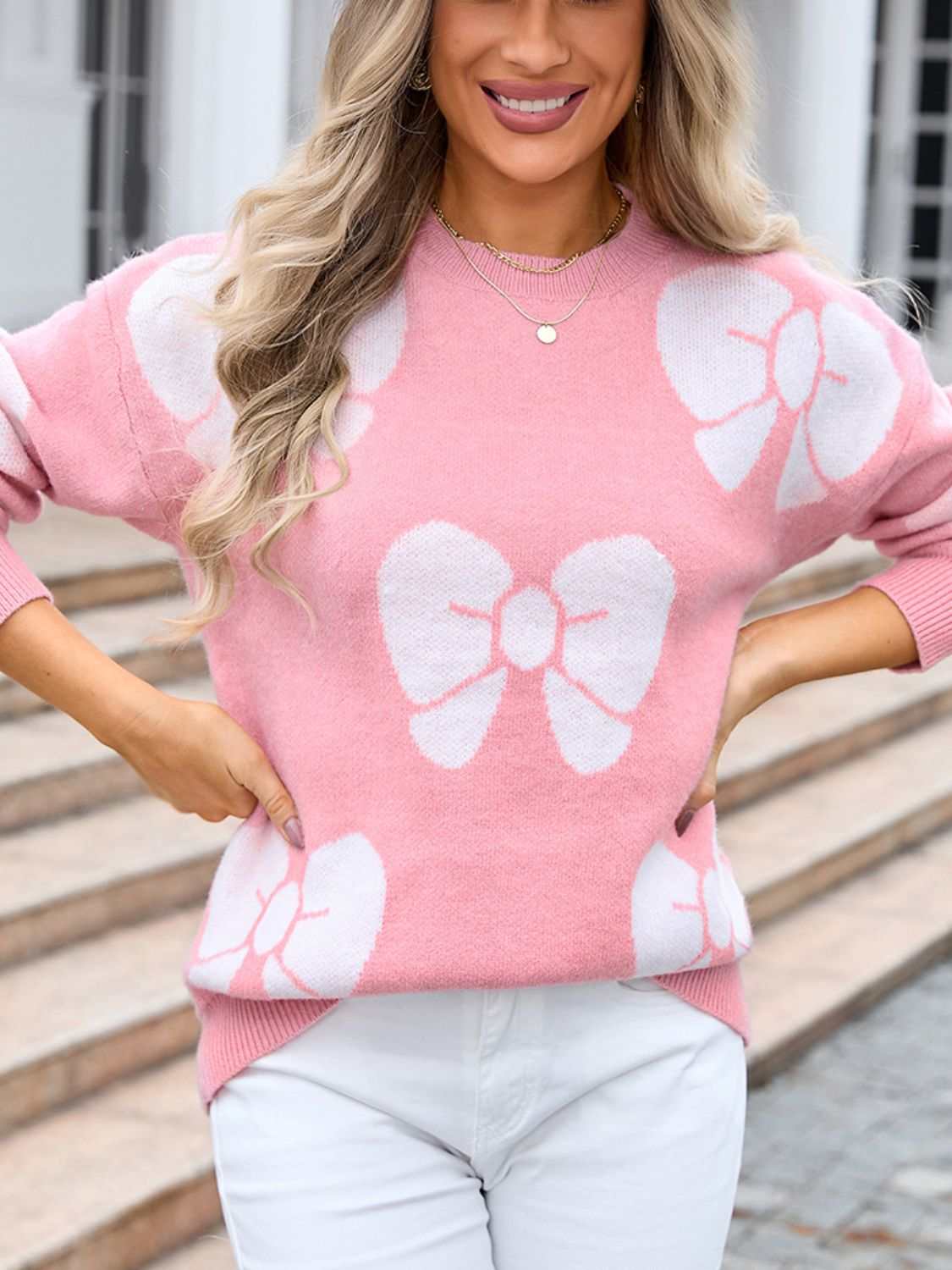 Pink sweater with white bow design, round neck, and dropped shoulders.