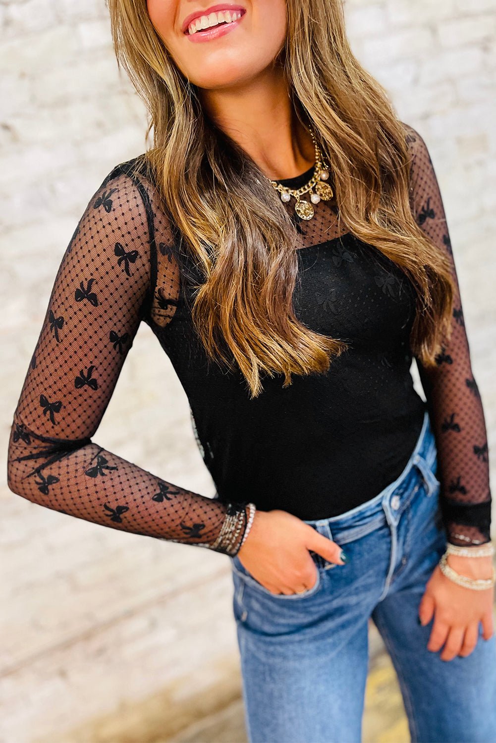 Woman wearing black bow pattern mesh long sleeve top with sheer sleeves and solid bodice paired with blue jeans