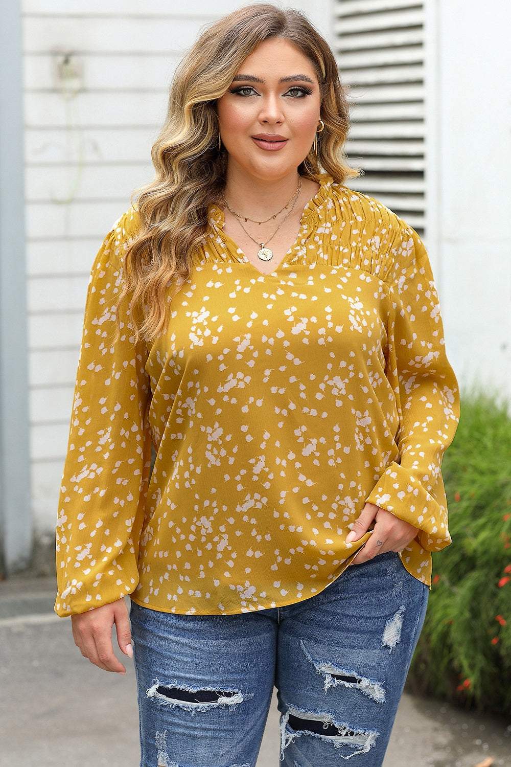 Plus size yellow notched neck smocked blouse with white pattern and long sleeves, paired with ripped blue jeans.