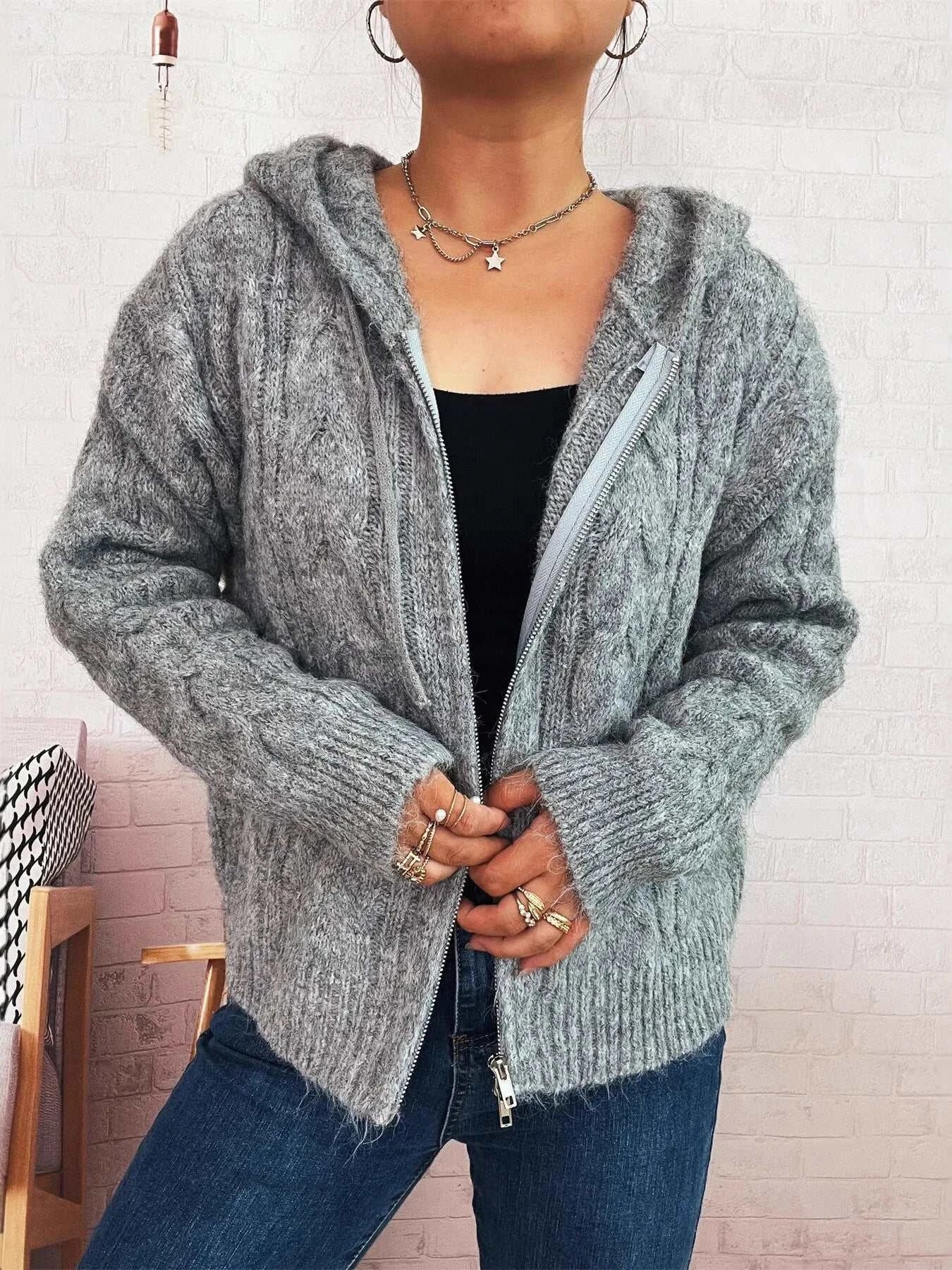 Grey cable knit hooded zip-up cardigan sweater with slight stretch, worn over a black top and blue jeans