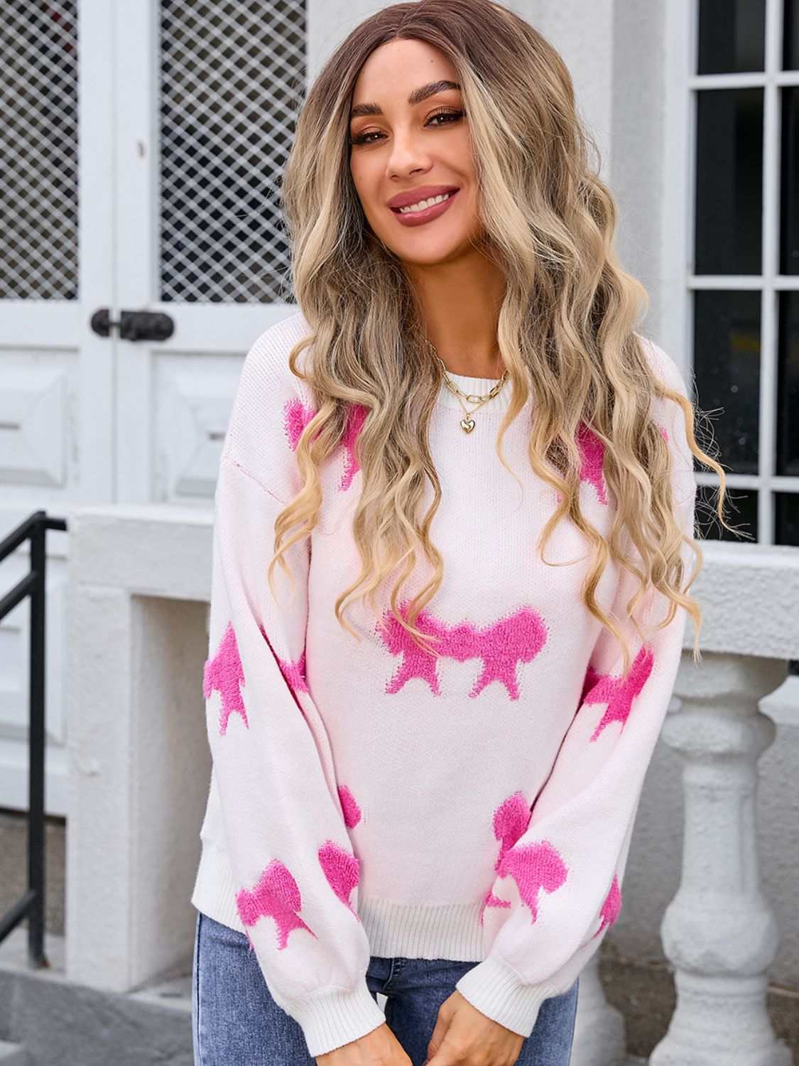 Angel Wings Bow Round Neck Dropped Shoulder Sweater in white with pink bow patterns, worn by a woman.