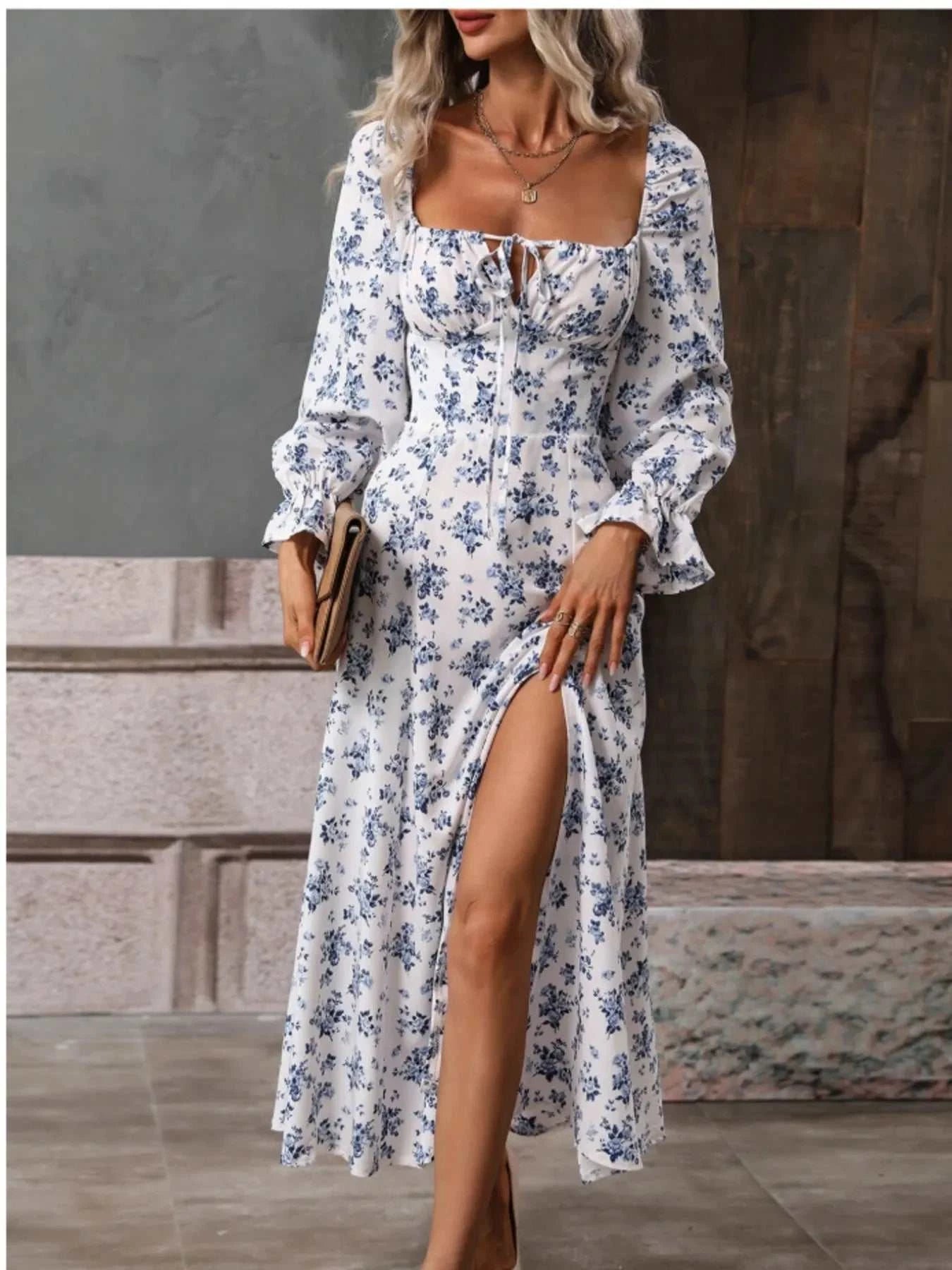 Woman wearing white floral print square neck dress with flounce sleeves and side slit holding clutch