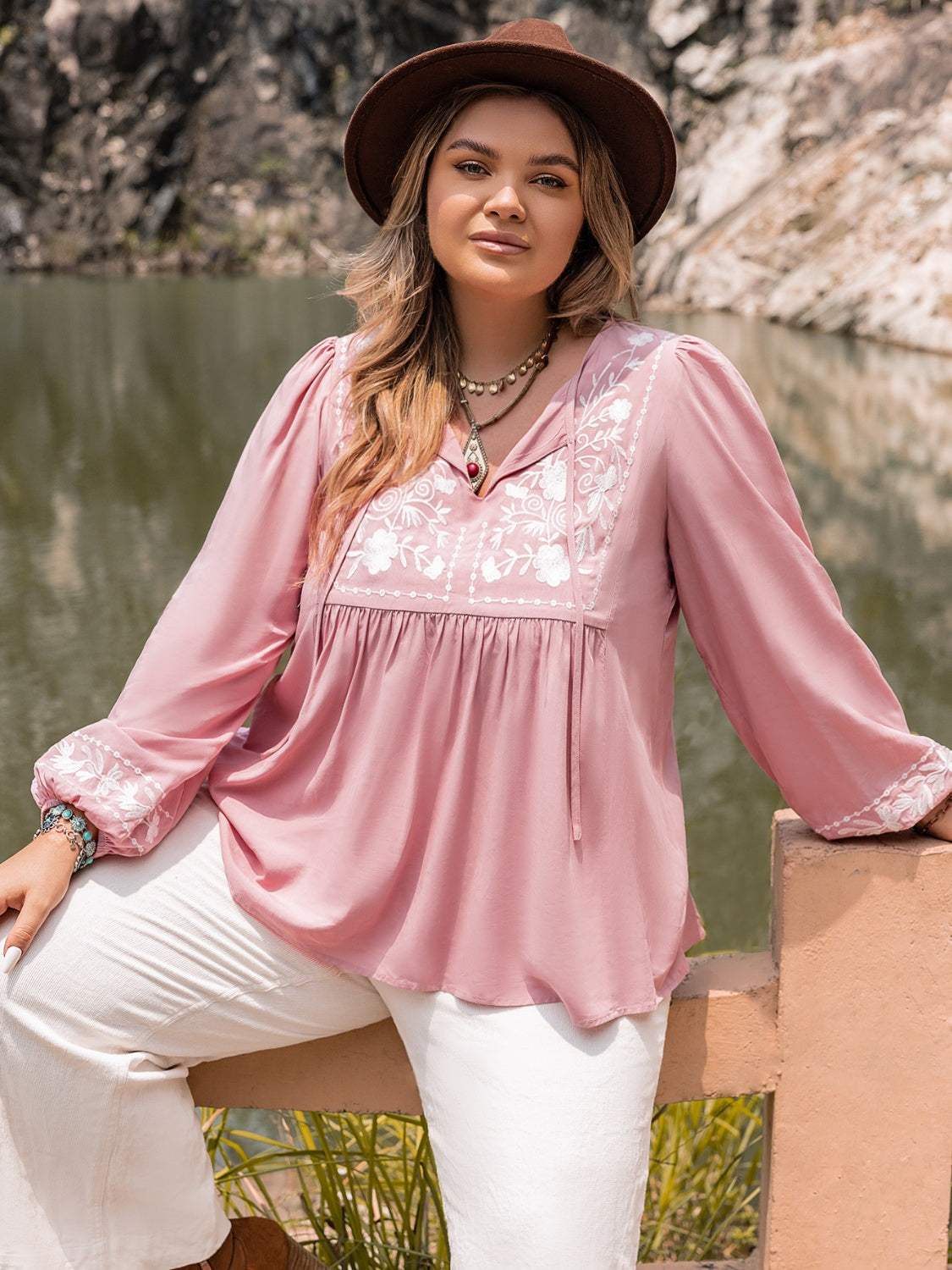Plus size pink tie neck puff sleeve blouse with embroidered front and white pants.