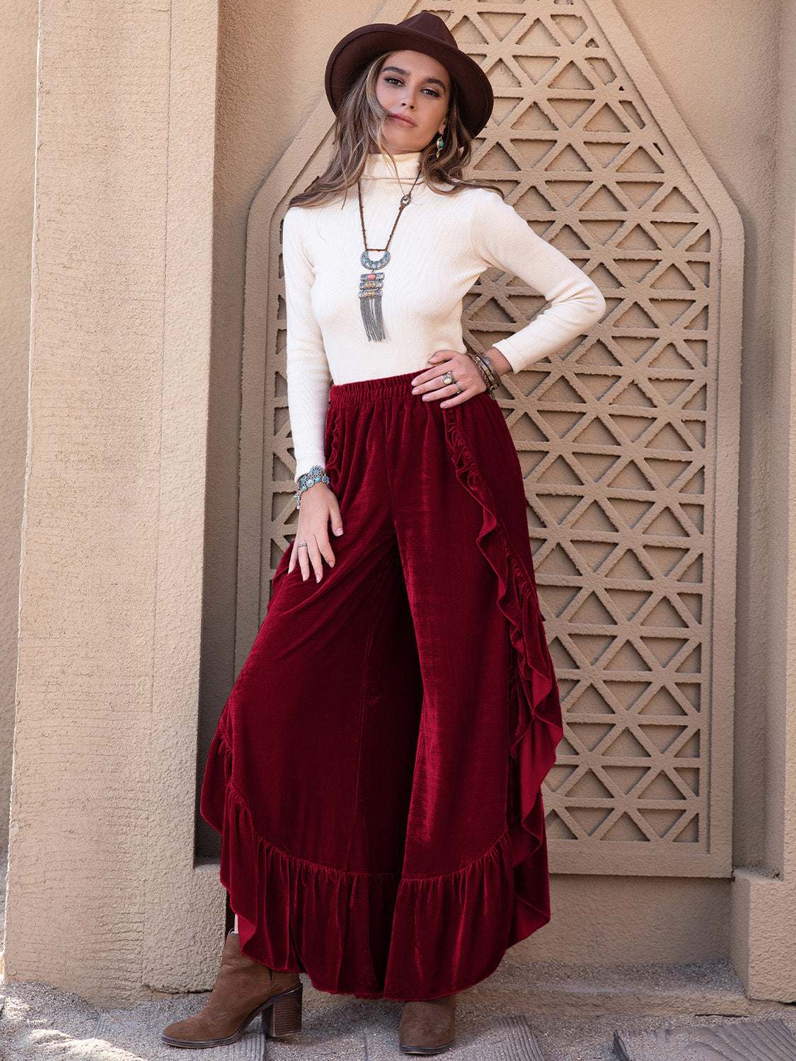 Woman wearing slit ruffled wide leg pants in red with a white top and brown hat.